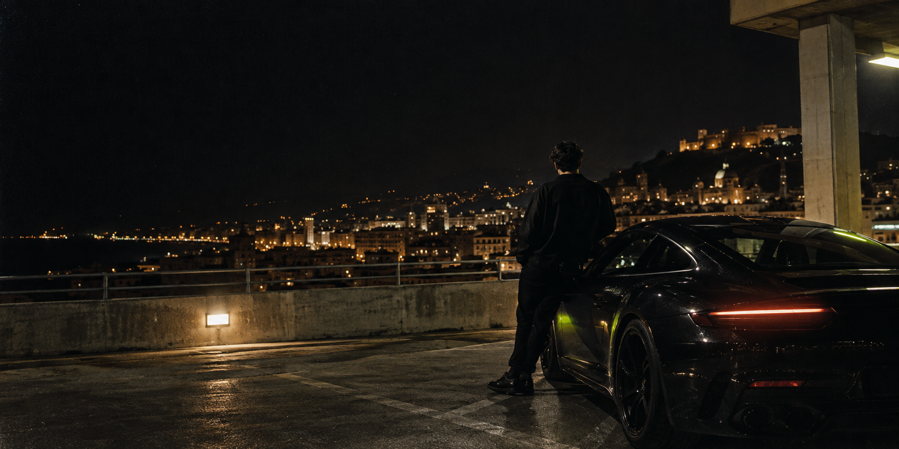 A person beside a black sports car overlooking a city at night